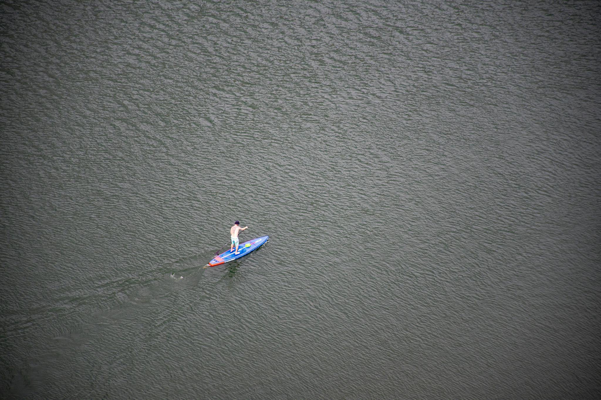 A lone paddler enjoying stand-up paddleboarding on serene ocean waters viewed from above.
