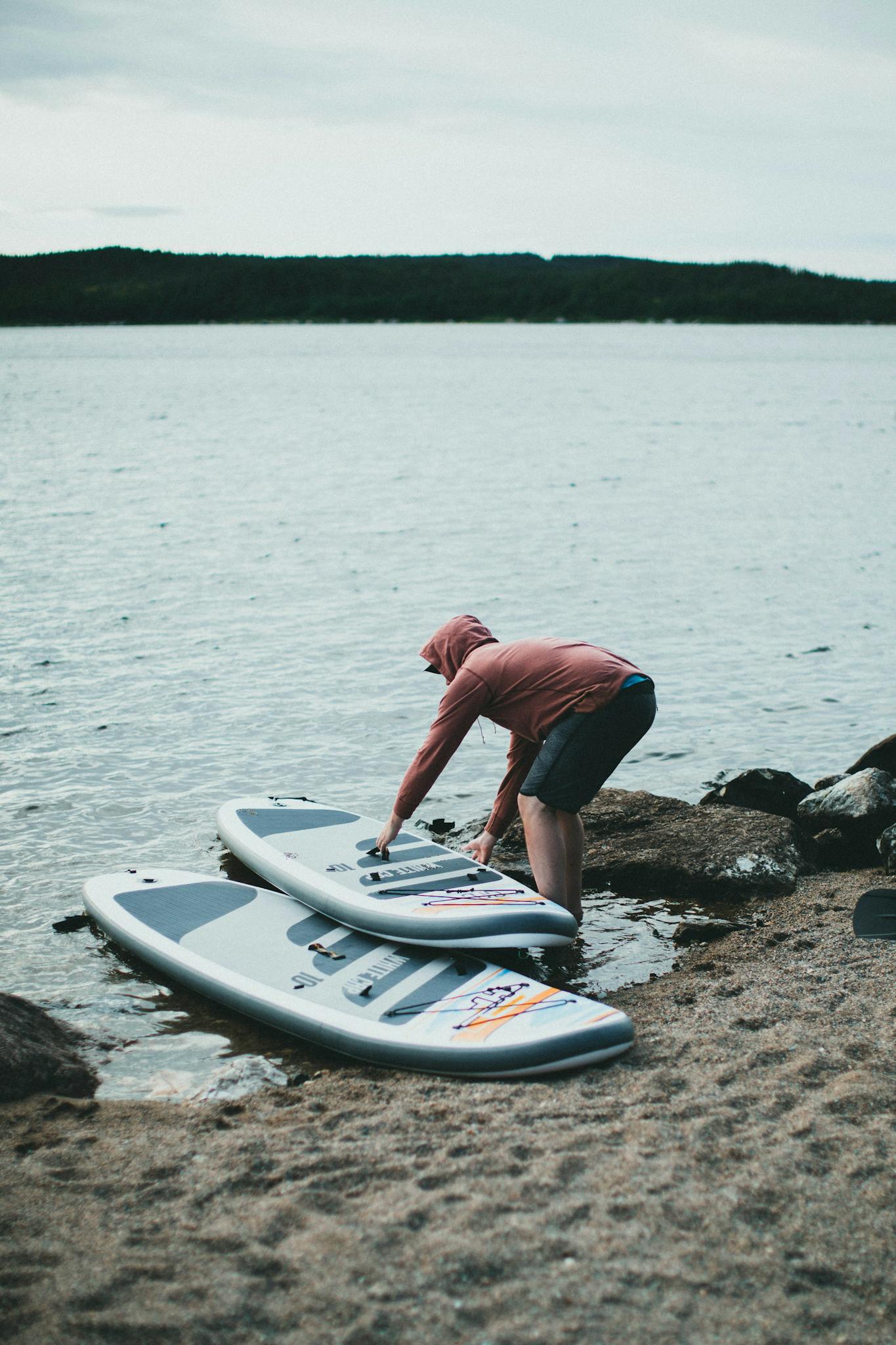 A person prepares paddle boards at the edge of a calm lake, showcasing outdoor recreation.