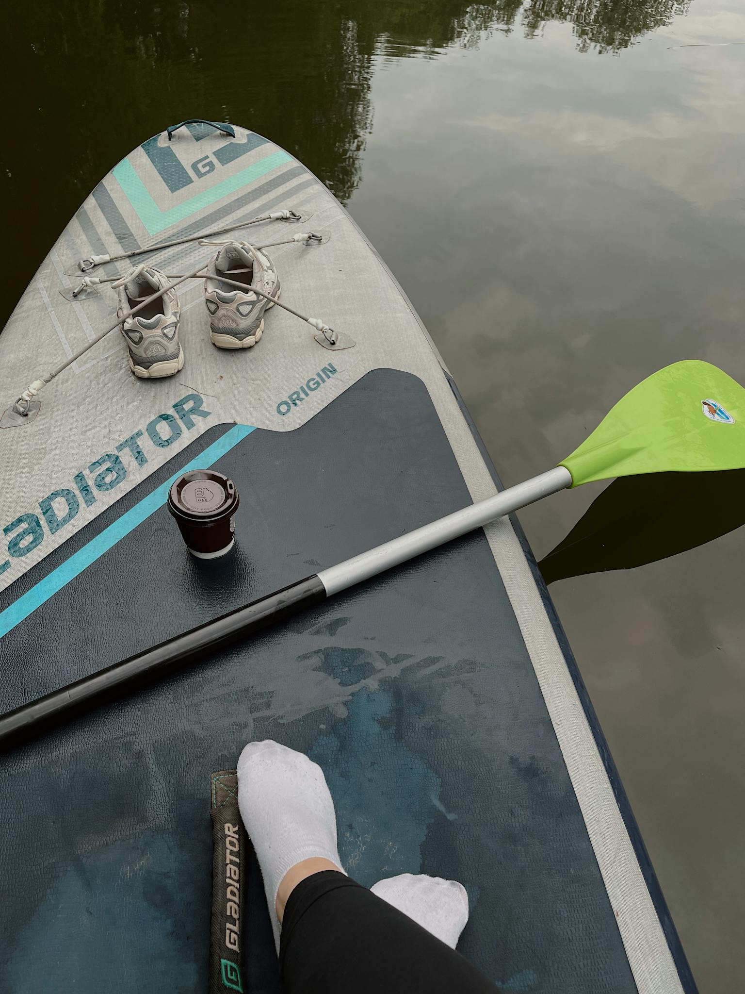 Relaxing paddleboard ride with gear on calm water, featuring vibrant paddle and sneakers.