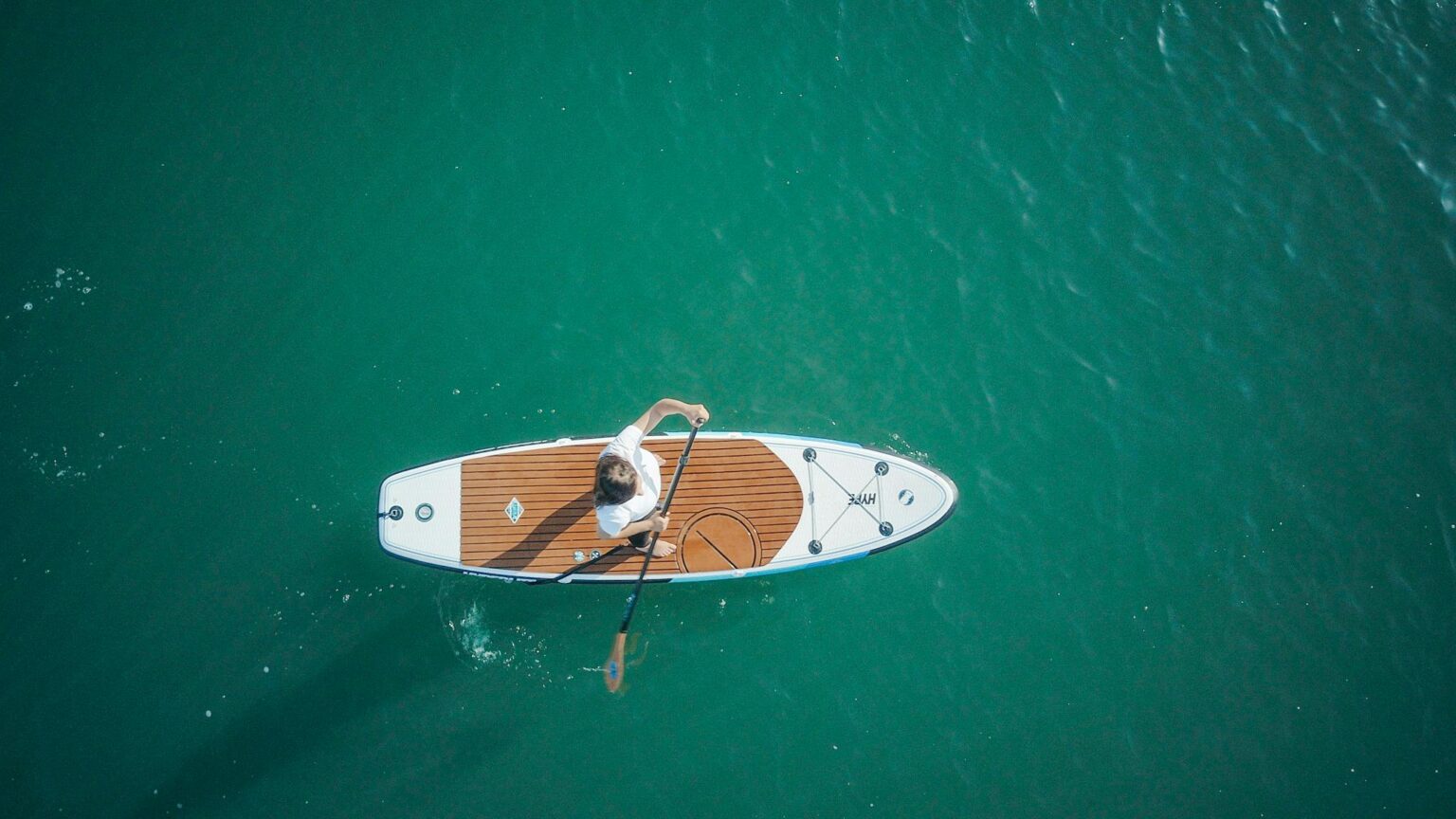 Aerial shot of an adult paddleboarding on serene turquoise water, enjoying a peaceful watersport activity.
